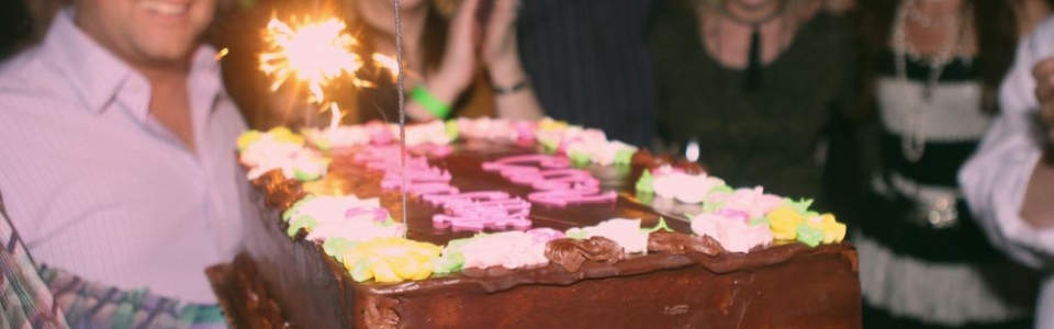 People standing around a lovely birthday cake with a sparkler